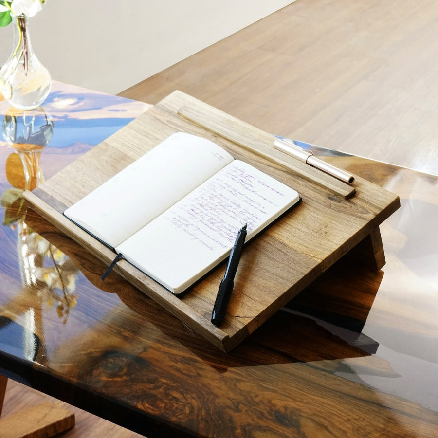 Masif ceviz laptop standı, üzerinde açık defter, epoksi masada çapraz yakın açı