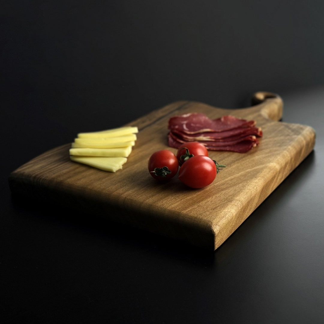 zeminde yatay konumda olan dogal masif ceviz ahsap kesme tahtasi bir sunum tahtasi gibi uzerinde taze domatesler ve kasar ile pastirma dilimleri bulunduruyor vornom