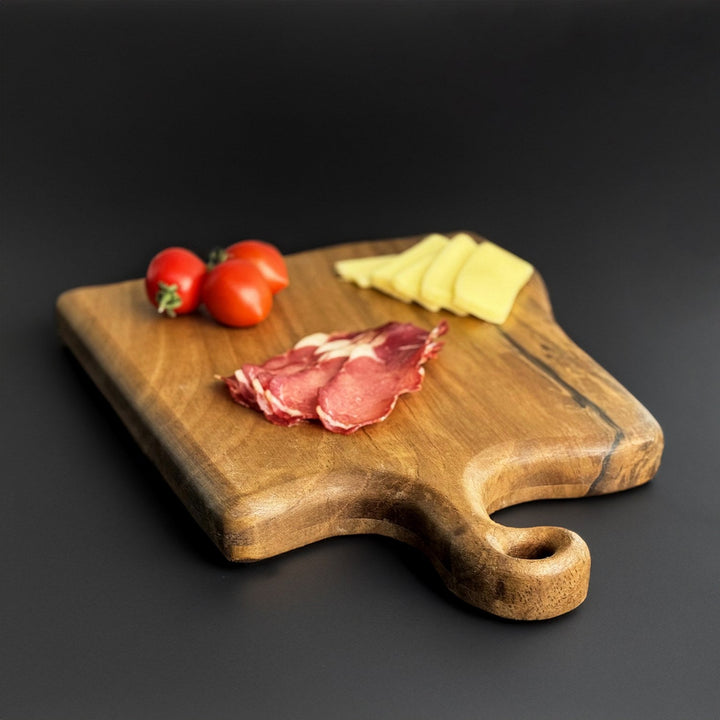 dogal masif ceviz ahsap kesme tahtasi uzerinde taze domatesler pastirma ve kasar peynir dilimleri yer almakta tahtanin sap kismi ozel bir tasarimla islenmis vornom