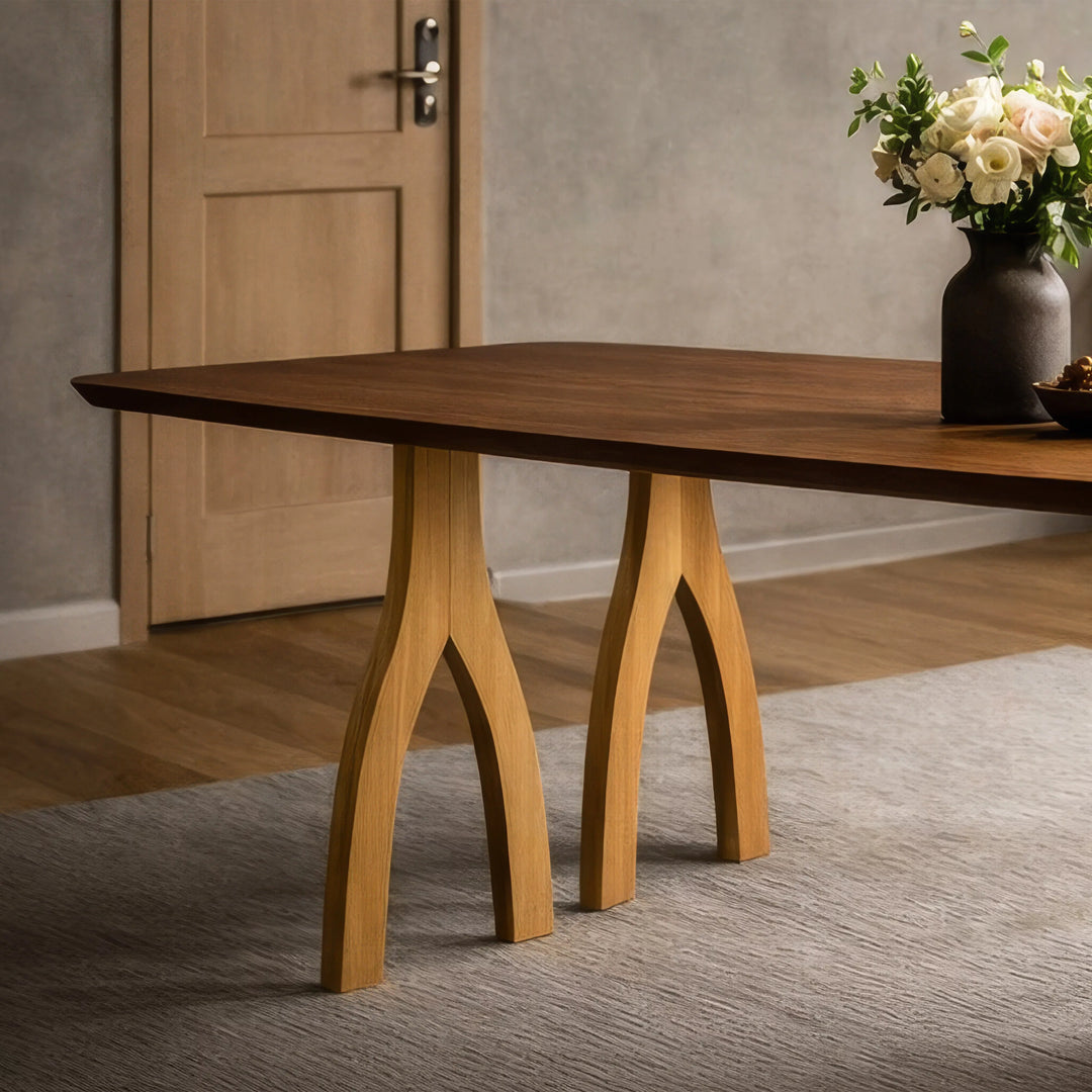 İki ayaklı, heykelsi tasarıma sahip kestane yemek masası üzerinde bir vazo yer alıyor.